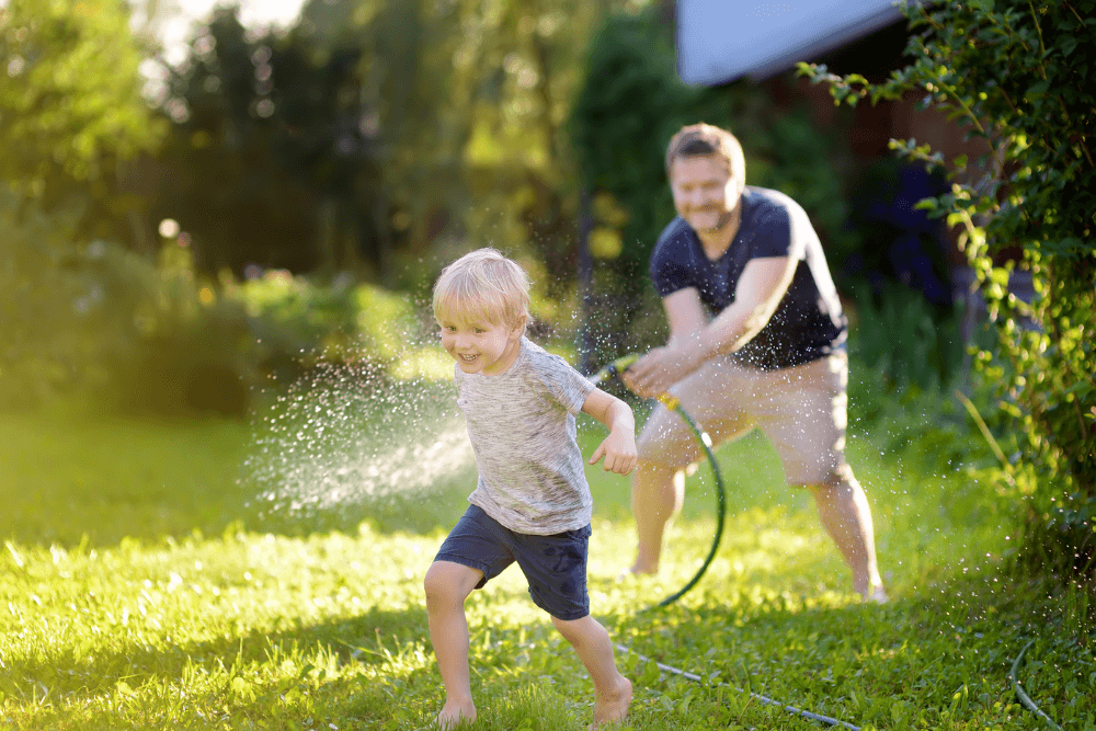 dad and son playing with water hose on a lush green lawn